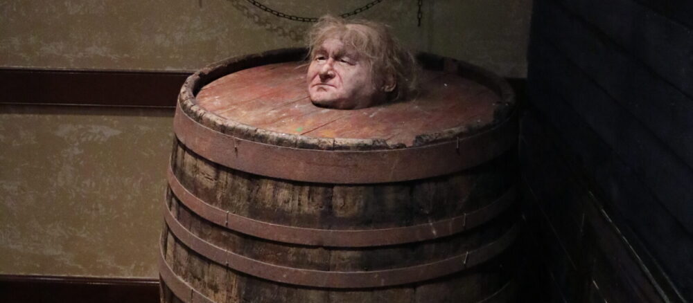 depiction of a medieval torture or punishment method, where a person is confined inside a wooden barrel with only their head exposed