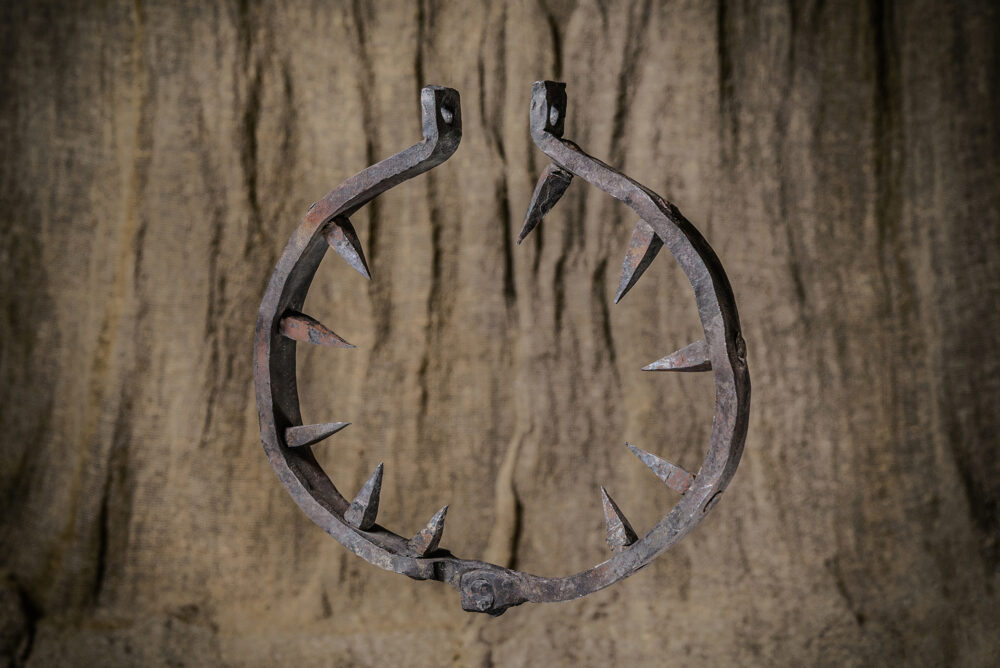 a spiked iron collar, a historical torture device, hanging against a wooden or textured backdrop.