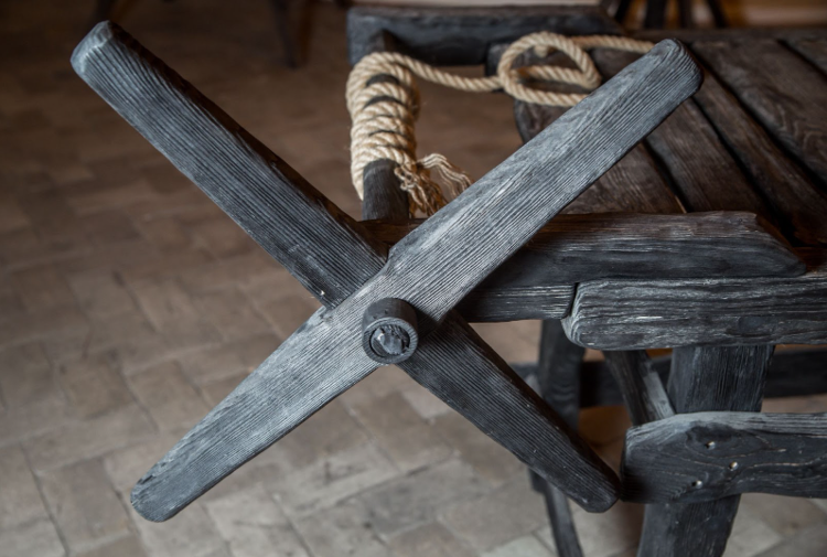 a wooden medieval torture device with a cross-shaped mechanism, accompanied by a rope, placed on a rustic wooden surface.