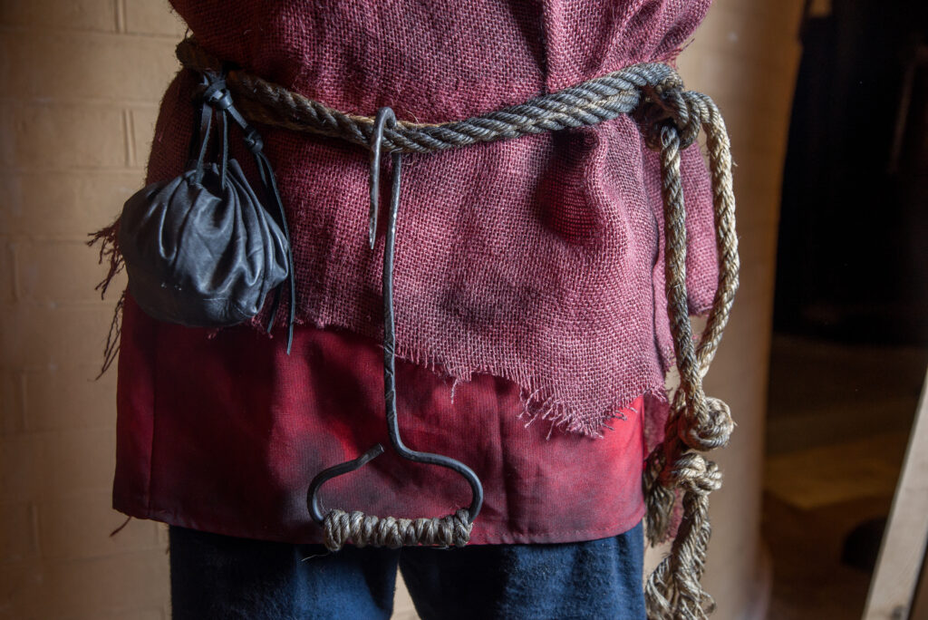 medieval-style outfit with a rope belt, a small pouch, and a metal hook accessory