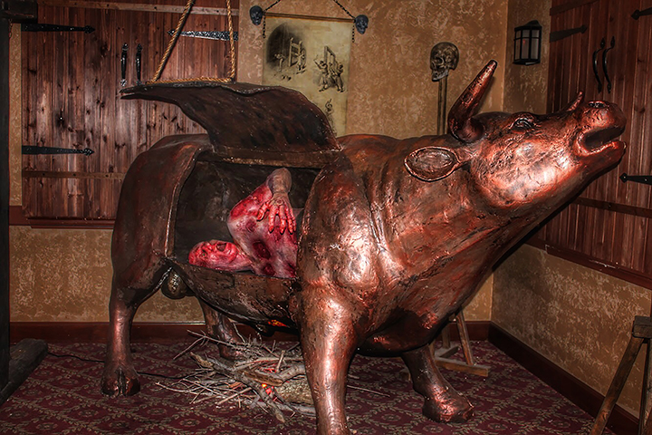 a bronze bull-shaped torture device, known as the "Brazen Bull," with its side open to reveal a human-like figure inside