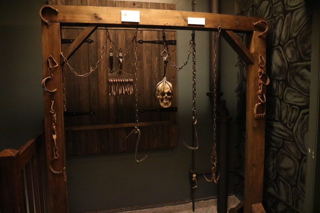 a wooden frame displaying medieval torture instruments, including hooks, chains, and a skull for decorative effect