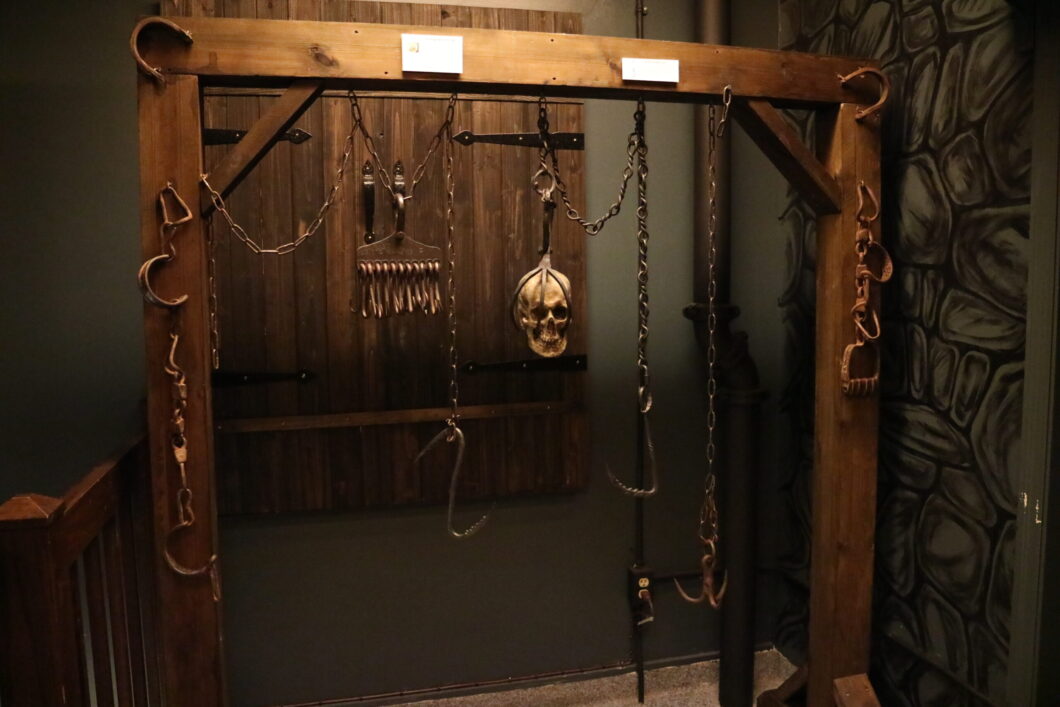 a wooden frame displaying medieval torture instruments, including hooks, chains, and a skull for decorative effect