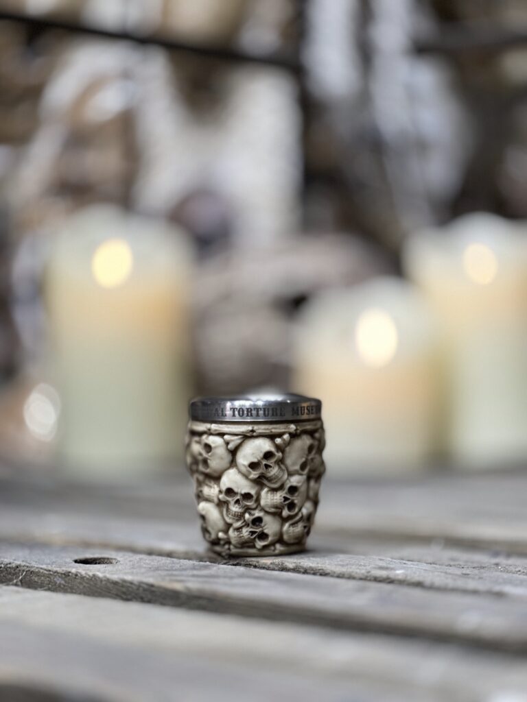 a small, metallic mug or cup adorned with a pattern of detailed skulls