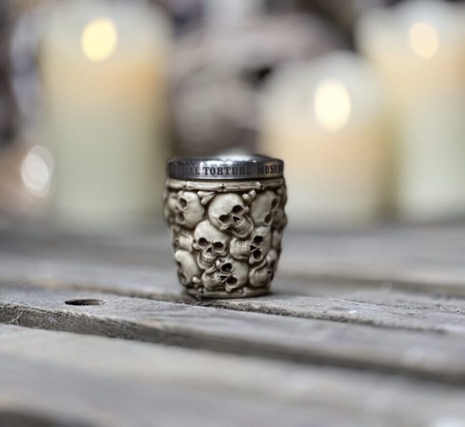 a small, metallic mug or cup adorned with a pattern of detailed skulls