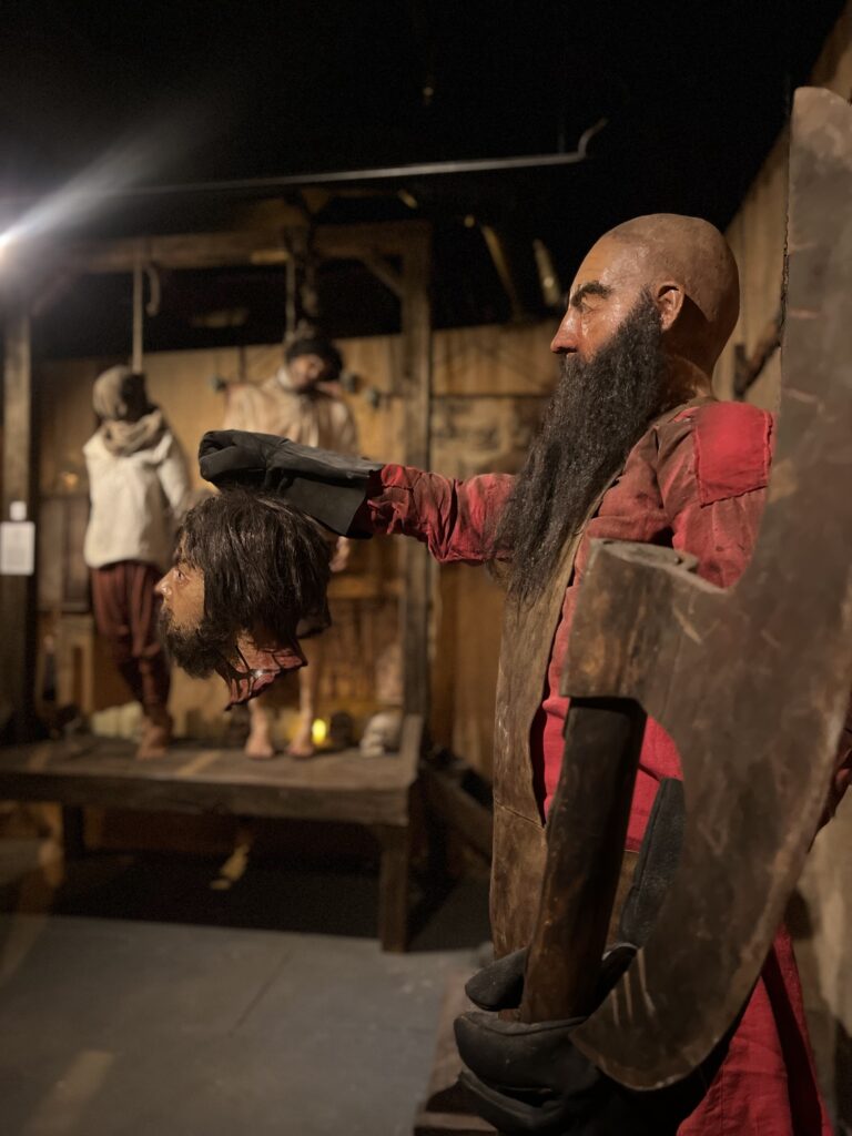 a medieval executioner holding a severed head in one hand, with an axe in the foreground